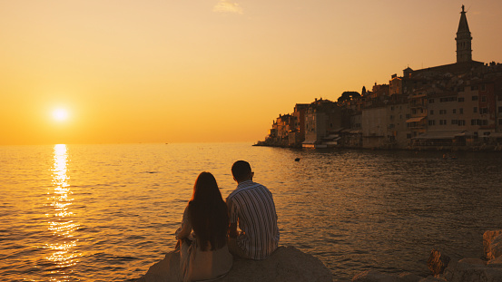 As the Sun Sets,Couple Sits Serenely on a Rock by the Ocean. Historic Town Bathed in the Golden Hues of Sunset. Tourists are Spending Leisure Time Together during Vacation.