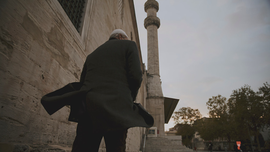 In the Timeless Cityscape of Istanbul,Turkey,a Rear View Captures a Mature Man Walking Outside a Mosque against the Backdrop of a Clear Sky. As he Moves Forward,the Elegant Architecture of the Mosque Stands Tall,Symbolizing Centuries of History and Tradition