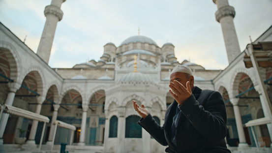 Captured From a Low Angle,a Mature Man Engages in Prayer Within the Serene Courtyard of the Blue Mosque,Set against the Vast Expanse of the Sky. His Devout Posture and Solemn Demeanor Epitomize the Essence of Spiritual Connection amidst the Majestic Surroundings of this Iconic Islamic Landmark at Istanbul,Turkey