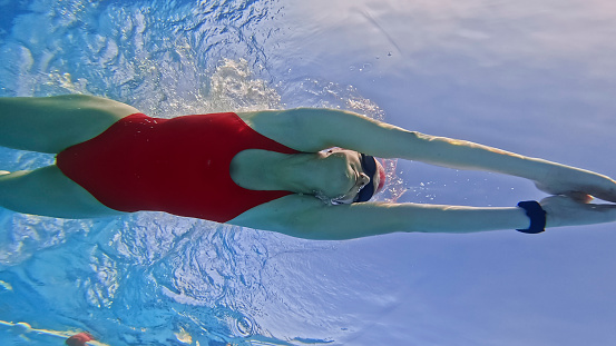 Skilled Female Swimmer,Dressed in a Vivid Red Swimsuit During Practice Sessions Dedicatedly Refining Her Swimming Techniques to Achieve Excellence Amidst the Tranquil Atmosphere of a Resort Pool.