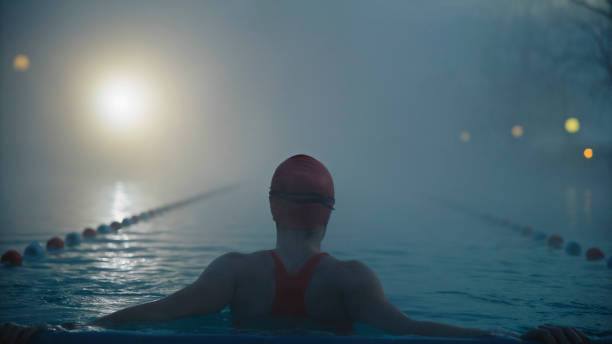 Rear view of Female Swimmer relaxing in Resort Pool at Misty Morning Amidst the Mist of a Tranquil Resort Morning,a Skilled Female Swimmer Enjoying the Calmness of the Resort Pool,Immersing Herself in the Soothing Embrace of Dawn. woman cold water swimming stock pictures, royalty-free photos & images