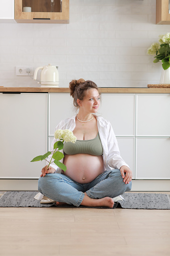 Eco pregnancy. Pregnant woman with big belly advanced pregnancy holding white flower hydrangea in hand at home. Healthy pregnancy and happy maternity