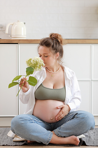 Eco pregnancy. Pregnant woman with big belly advanced pregnancy holding white flower hydrangea in hand at home. Healthy pregnancy and happy maternity