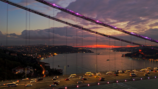 From a High Angle,Vehicles Traverse the Illuminated Bosphorus Bridge over the Marmara Sea against a Backdrop of Cloudy Skies at Dusk in Istanbul,Turkey. The Bridge's Lights Cast a Radiant Glow,Contrasting with the Deepening Hues of the Evening Sky