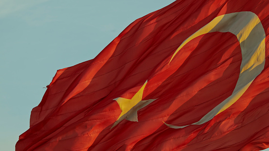 The Vibrant Red Turkish Flag Flutters Gracefully against the Backdrop of a Clear Sky in Istanbul,Turkey. The Low Angle View Captures its Proud Display,Symbolizing the Nation's Strength and Unity Under the Bright Daylight