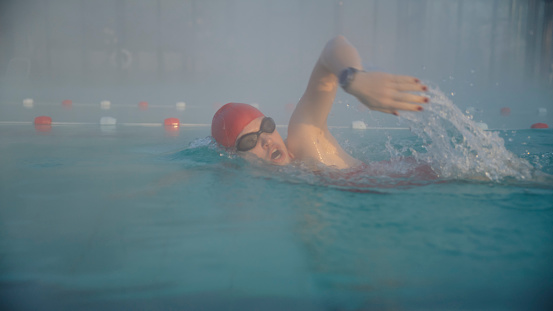 A Skilled Female Swimmer Gracefully Refining Her Swimming Strokes,Creating a Serene Ambiance for Her Dedicated Practice Session in the Tranquil Mist of Early Morning.
