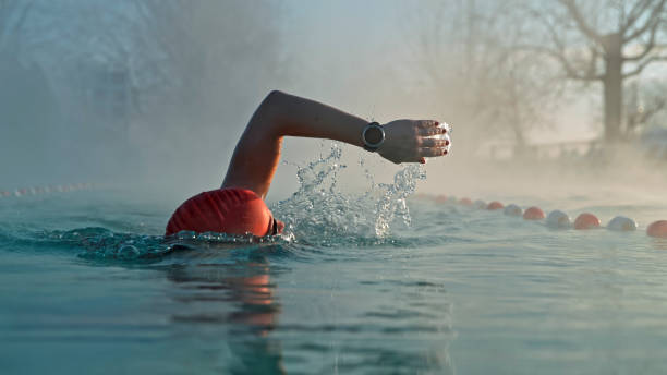 Lady Perfecting Swimming Strokes in Foggy Pool Setting Proficient Lady Refining Her Swimming Technique,Showcasing Commitment and Perseverance in the Peaceful Pool Environment Amidst the Foggy Ambiance of Dawn. woman cold water swimming stock pictures, royalty-free photos & images