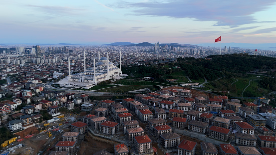 The Aerial Mid Distance View Showcases the Enchanting Blue Mosque Set amidst a Bustling Residential District during the Captivating Sunset Hours. As the Golden Hues of Dusk Envelop the Scene,The Mosque's Majestic Domes and Minarets Stand Out against the Backdrop of the Crowded Urban Landscape