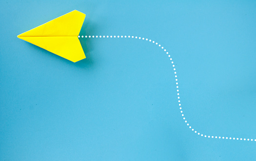 Top view of yellow paper airplane making turning on blue background.