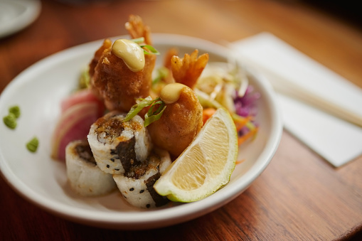 Food, sushi and poke bowl on table at restaurant for gourmet, healthy and wellness meal. Diet, ingredients and culinary Chinese dish on plate with seafood, sauce and lemon in cafeteria or diner.