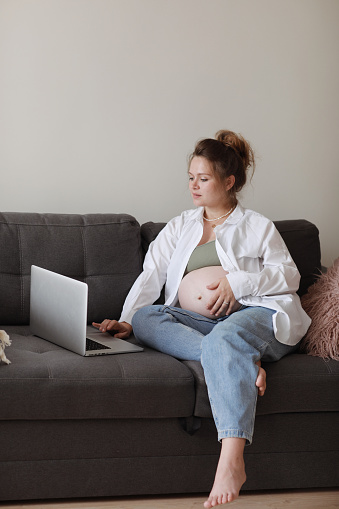 Attractive pregnant young lady working remotely online from home office. Close up woman hands on laptop with big belly advanced pregnancy. selective focus