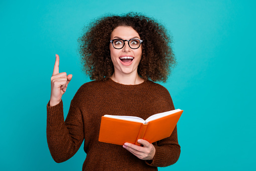 Portrait of young excited funky woman student with copybook point finger up shocked found correct formula isolated on cyan color background.