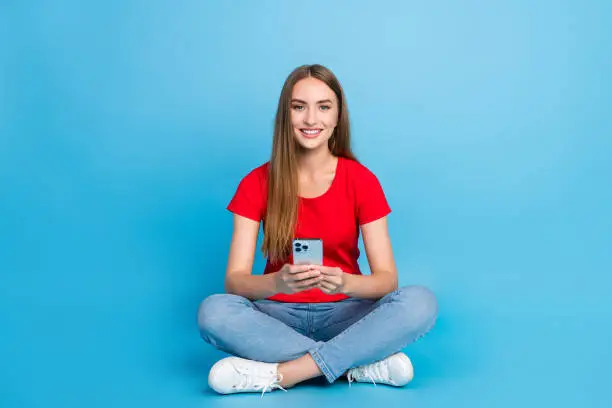 Photo of cheerful charming girl sitting using modern samsung chatting online isolated on blue color background.