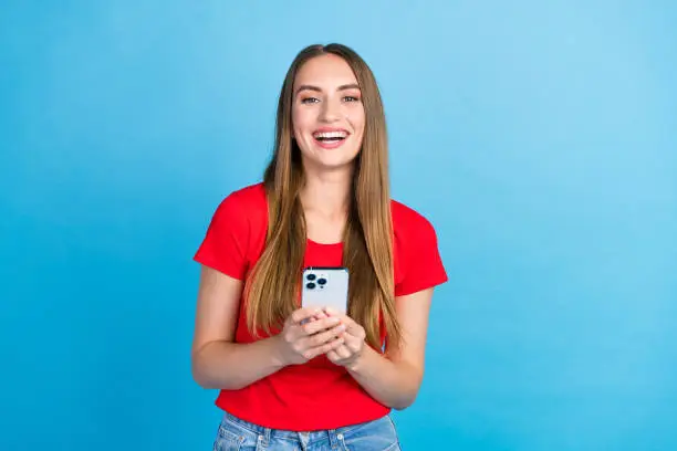 Photo of Photo of positive adorable girl influencer popular blogger use modern device apple iphone isolated on blue color background