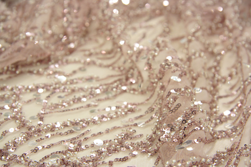 Pink decorated fabric. Intricate beaded and sequined ornaments. Bokeh effect, defocused. Natural shimmering