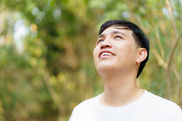 Happy delighted Asian adult age man enjoy in the nature environment in forest  with beautiful sunlight behind the trees. Leisure activity with a nature concept. Delightful Asian man relaxing alone in the nature environment portrait.