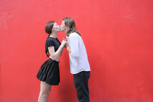 A couple is enjoying a summer vacation in the red wall background, happily showing their love to each other.