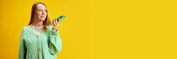 istock Banner. Young woman using smartphone and speaking by cellular connection against yellow studio background with negative space against studio background. 2025467213