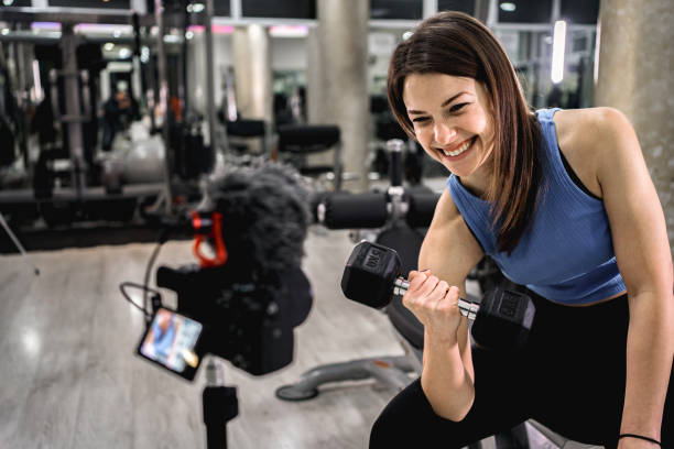 istock White woman filming a tutorial in the gym while doing biceps curl with dumbbell 2025521664
