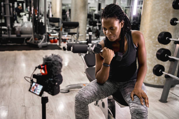 istock Black woman filming a tutorial in the gym while doing biceps curl with dumbbell 2025521674