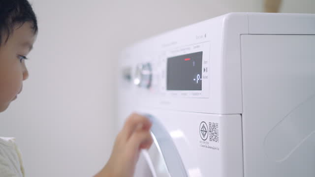 Cute little boy doing laundry at home.Press the start button of the dryer.