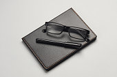 Notebook with black leather cover and pen, eyeglasses on gray background. Business concept.