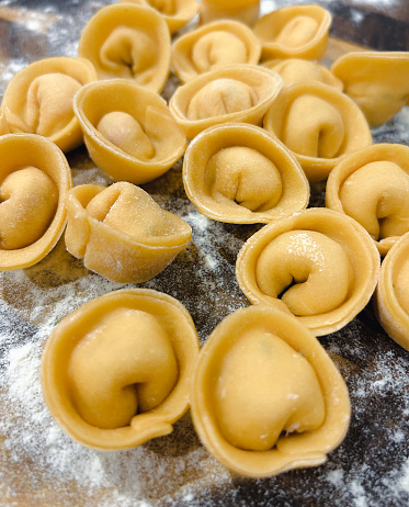 Multiple freshly made, rustic handcrafted pasta tortellini with delicious filling, sat on a wooden board and dusted with flour.