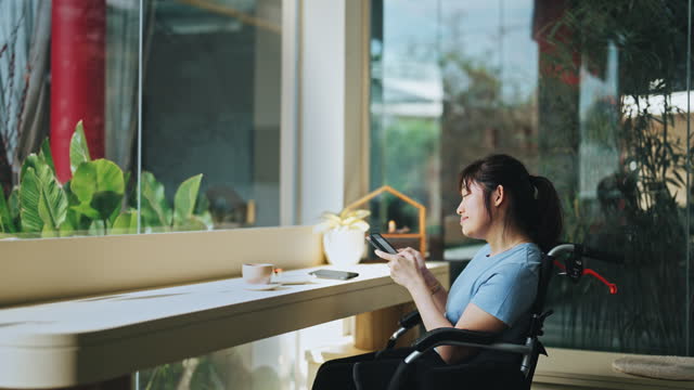 Asian Chinese cerebral palsy woman in wheelchair reading text messages in cafe weekend morning