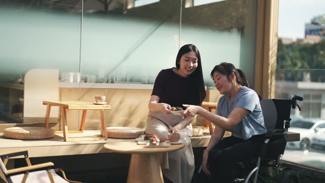 Social Gathering Happy Asian Chinese cerebral palsy woman in wheelchair with friend in front of Japanese cafe weekend morning