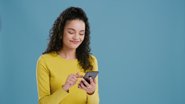 Woman, surprise with smartphone and social media, happy with announcement online for winning on blue background. Energy, dancing and scroll internet with wow reaction, giveaway or lotto on mobile app