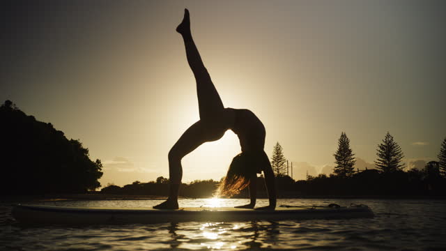 Young Beautiful Fit woman Practicing Paddle Board yoga at sunset