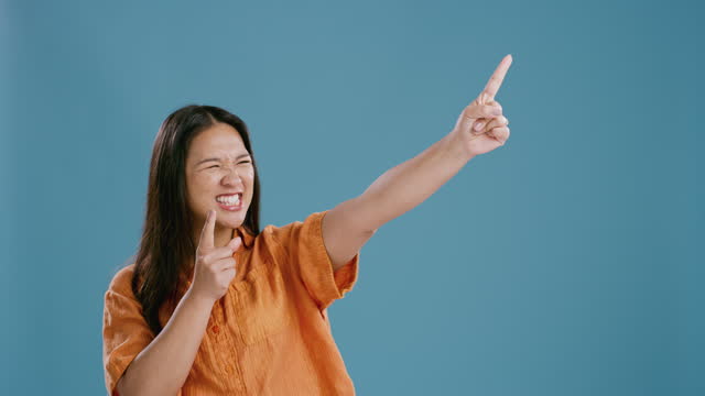 Wow, cheering and excited asian woman with hand pointing to mockup in studio celebration on blue background. Winner, announcement or Japanese model show competition giveaway, prize or goal motivation