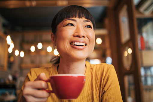 Close-up portrait of a Japanese woman. He is holding a cup of coffee and looking happy.