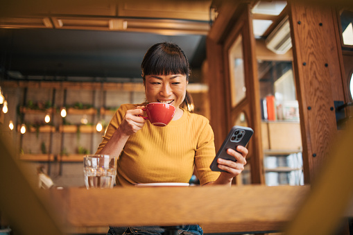 Japanese woman drinking coffee and using her smartphone.