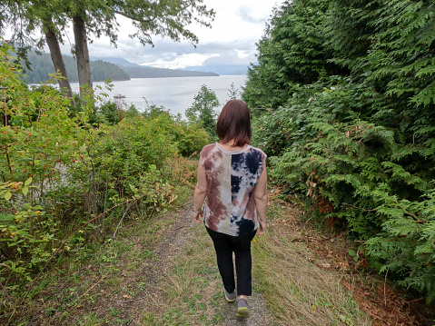 Woman walks down pathway through forest to ocean