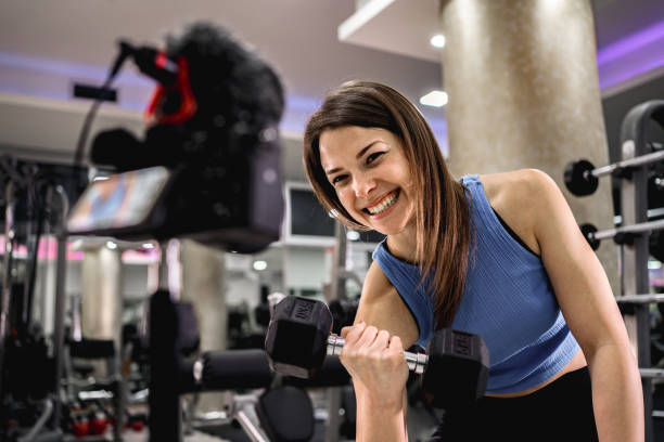 istock White woman filming a tutorial in the gym while doing biceps curl with dumbbell 2025665224