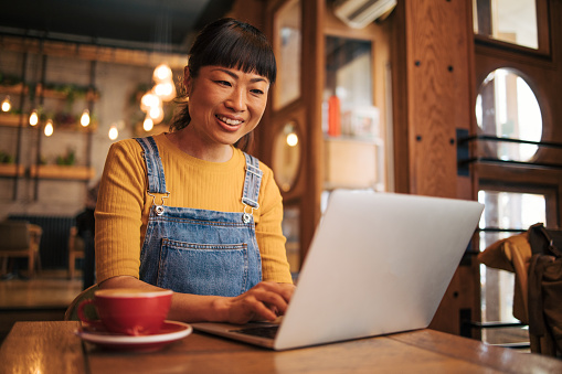 Japanese woman working on her laptop in a coffee bar. He looks very happy.