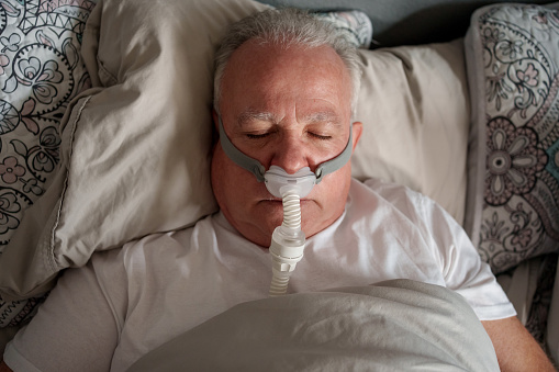 Mature Man Sleeping with a CPAP (Continuous positive airway pressure) Machine after being diagnosed with Sleep Apnea