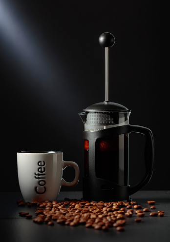 French press coffee and a cup on a black table with coffee beans.