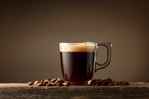 Espresso coffee glass cup on a brown background. Coffee cup and roasted coffee beans on a old wooden board. Copy space.