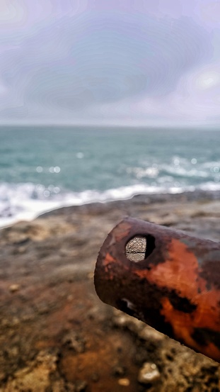A close-up shot of a rusty metal cylinder on a rocky bay in the Western Black Sea shores of Turkey. The season is winter and the wheather is rainy with dark clouds.