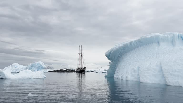 retro style sailing schooner during the huge iceberg in the Antarctic peninsula at the South Pole, waves of the southern ocean in cloudy weather