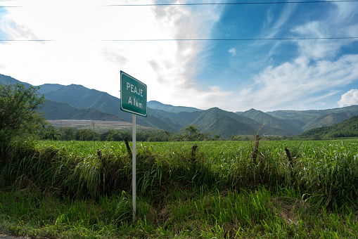 Toll announcement sign on a Colombian highway with a tropical climate.