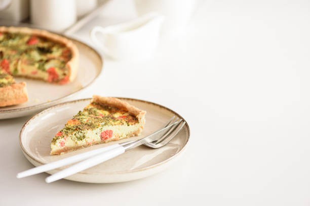 The pizza has a golden crust and is topped with melted cheese and basil leaves. One slice is partially removed, revealing the thick, cheesy interior. The wooden table beneath has a natural, rustic texture. A set of cutlery is placed on the table beside the board.