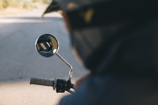 A biker in a helmet and protective glasses is reflected in the mirror of his motorcycle.