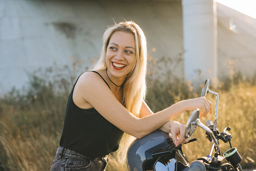 Biker girl sits on a motorcycle. Young beautiful blonde woman sitting on a motorcycle on the highway at sunset.