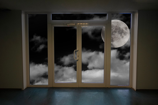 full moon in the clouds in the dark sky behind a closed window