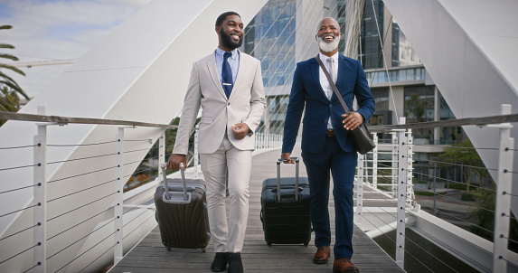 Business, travel and people with luggage outdoor at airport or walking to hotel together. Professional, men and African businessman moving on sidewalk with suitcase, bag or journey on road in city