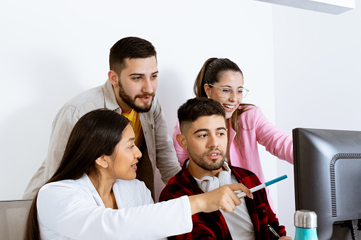 Multiethnic group of young workers in front of a PC. Brunette woman points at the screen. Youth at work concept.