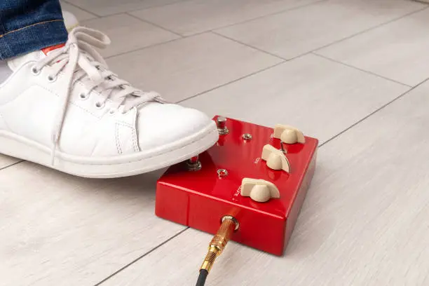 A musician's foot pressing an red effects pedal during a performance at home.